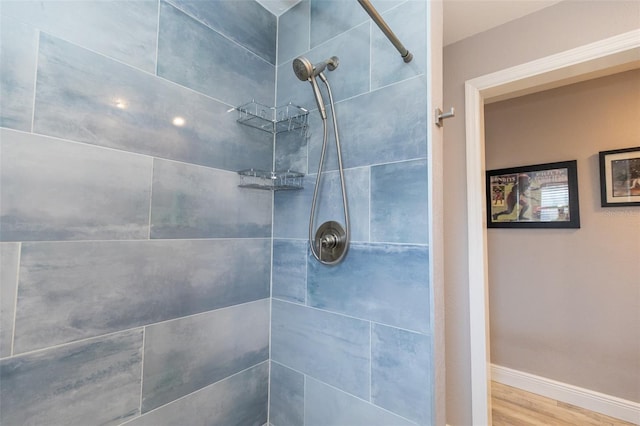 full bath with a tile shower, wood finished floors, and baseboards