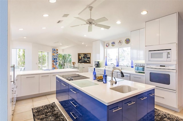 kitchen with modern cabinets, a sink, blue cabinets, white appliances, and a center island with sink