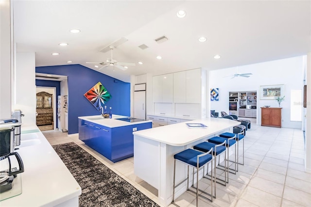 kitchen featuring visible vents, an island with sink, a ceiling fan, and vaulted ceiling