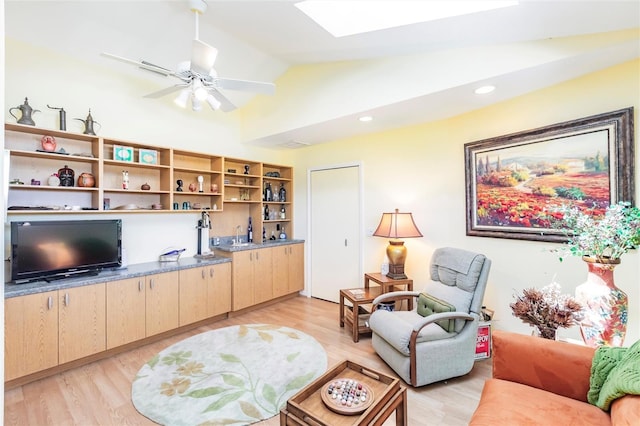 living area featuring a ceiling fan, light wood-style floors, and lofted ceiling with skylight