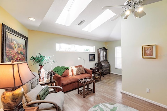 living room with vaulted ceiling with skylight, light wood-type flooring, a ceiling fan, visible vents, and baseboards