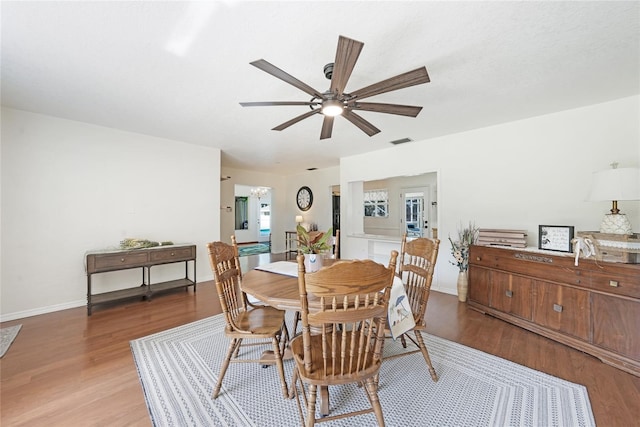 dining space with a ceiling fan, visible vents, wood finished floors, and baseboards