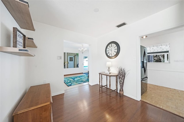 hall featuring wood finished floors, a chandelier, and visible vents