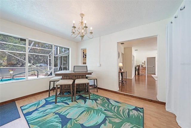 dining space with a textured ceiling, wood finished floors, a notable chandelier, and baseboards