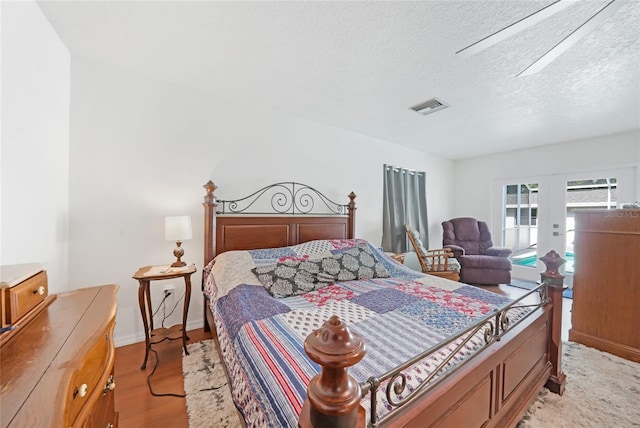 bedroom featuring a textured ceiling, visible vents, light wood finished floors, and baseboards