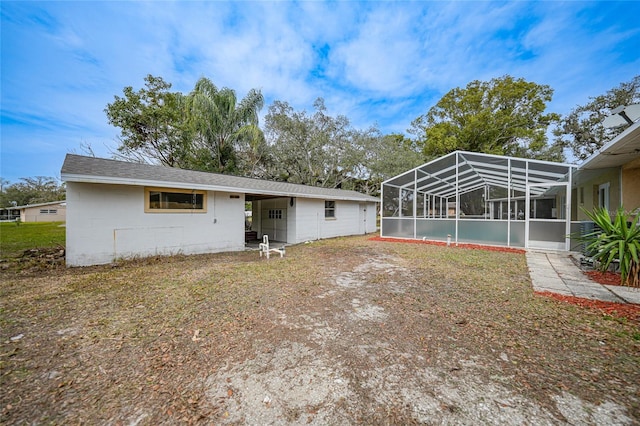 rear view of property with a shingled roof, concrete block siding, and a lanai