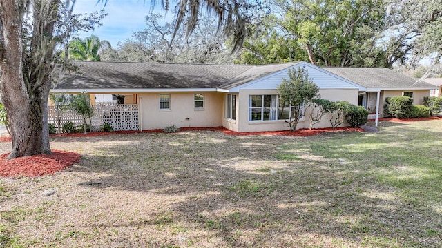 rear view of house featuring a yard, stucco siding, and fence
