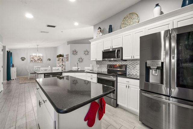 kitchen with a sink, decorative backsplash, a notable chandelier, white cabinets, and appliances with stainless steel finishes