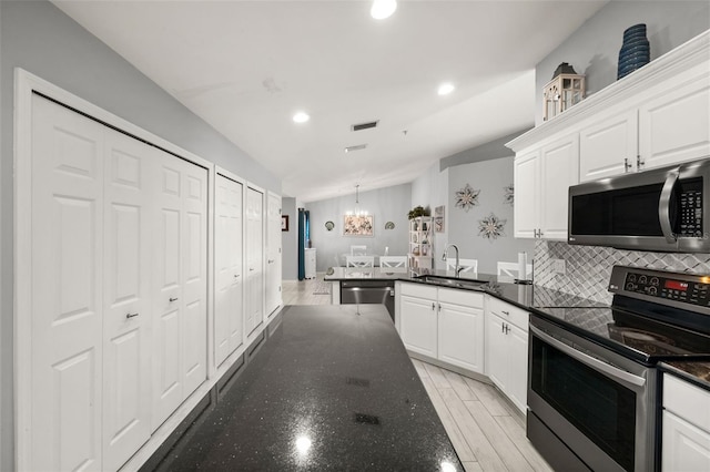 kitchen with appliances with stainless steel finishes, white cabinets, backsplash, a sink, and a peninsula