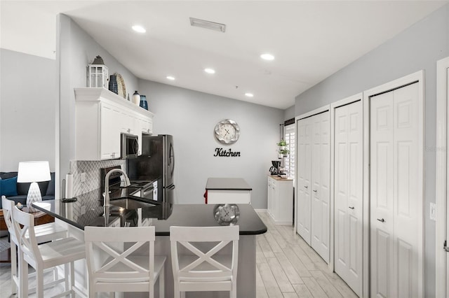 kitchen featuring light wood-style flooring, stainless steel appliances, dark countertops, white cabinetry, and visible vents