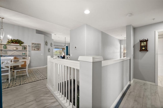 corridor with an upstairs landing, a chandelier, wood finished floors, and baseboards
