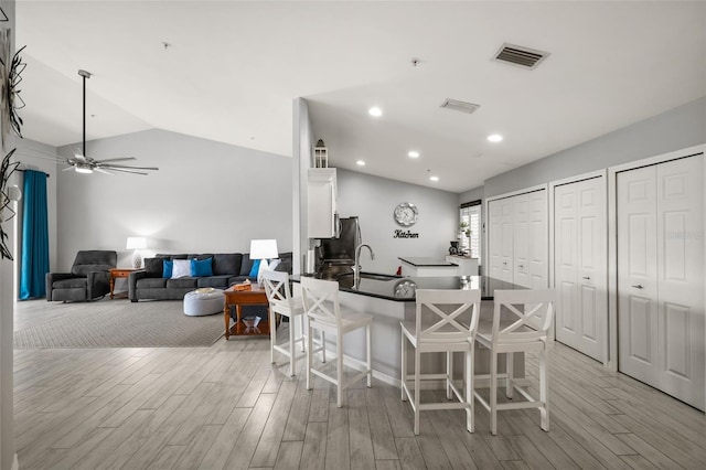 kitchen featuring a kitchen bar, white cabinetry, vaulted ceiling, and light wood-style floors