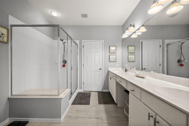 bathroom with baseboards, a shower stall, double vanity, and a sink