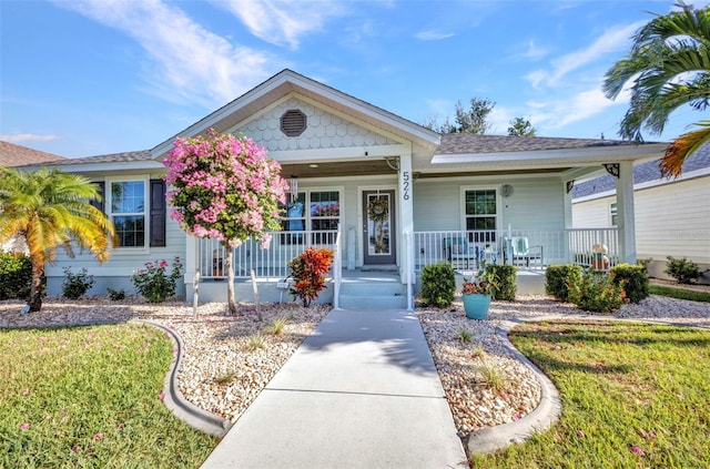 view of front facade featuring a front lawn, a shingled roof, and covered porch