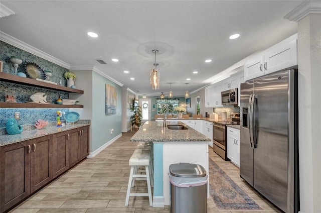 kitchen with light stone countertops, appliances with stainless steel finishes, white cabinets, ornamental molding, and a sink