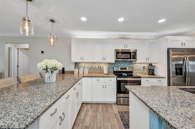 kitchen featuring light wood finished floors, stainless steel appliances, backsplash, ornamental molding, and white cabinets