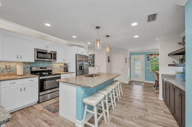 kitchen featuring wood finish floors, appliances with stainless steel finishes, crown molding, and a sink