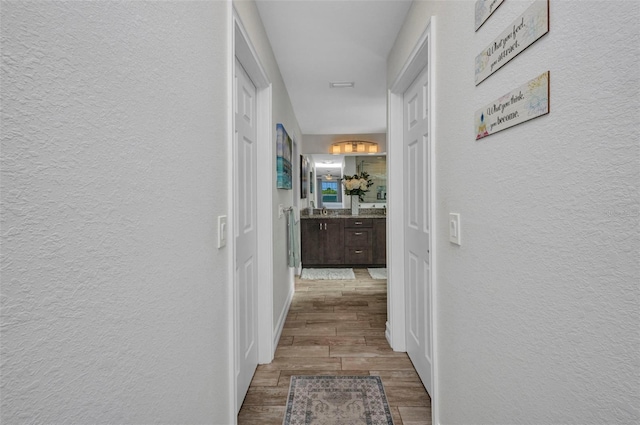 hall with a textured wall, wood finished floors, and baseboards