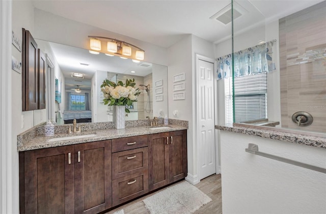 bathroom featuring wood finished floors, a tile shower, visible vents, and a sink
