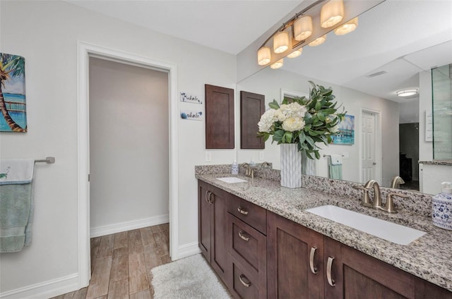 full bathroom with a sink, double vanity, visible vents, baseboards, and wood finished floors
