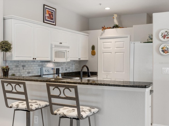 kitchen with dark stone counters, decorative backsplash, white cabinets, stove, and white microwave