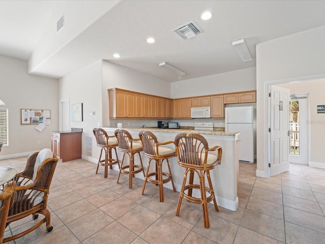 kitchen featuring visible vents, white appliances, a peninsula, and a kitchen breakfast bar