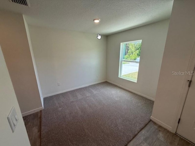 unfurnished room featuring visible vents, a textured ceiling, carpet, and baseboards
