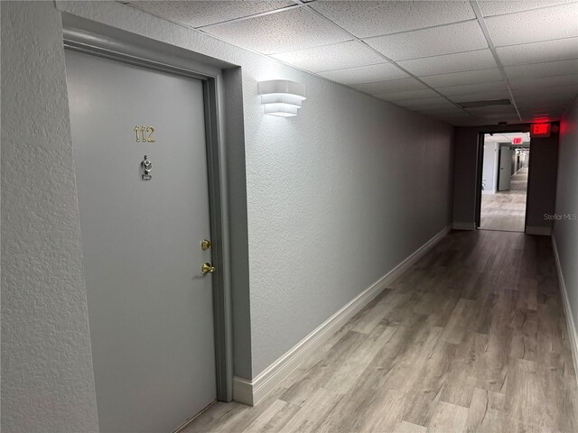 corridor featuring baseboards, a textured wall, wood finished floors, and a drop ceiling