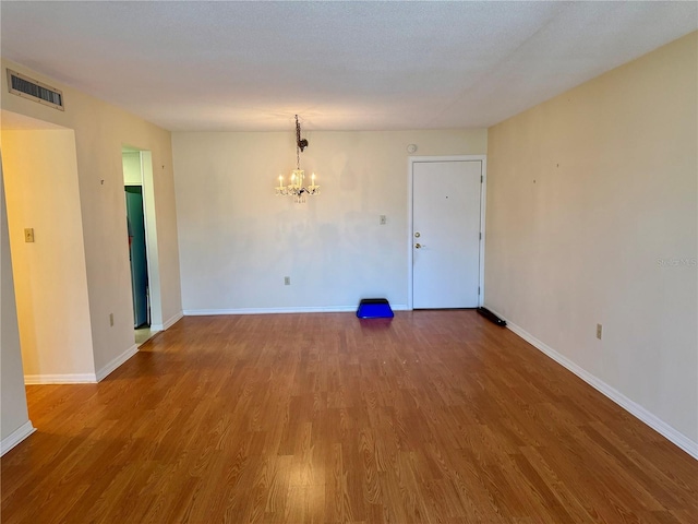 spare room with baseboards, visible vents, wood finished floors, and a notable chandelier