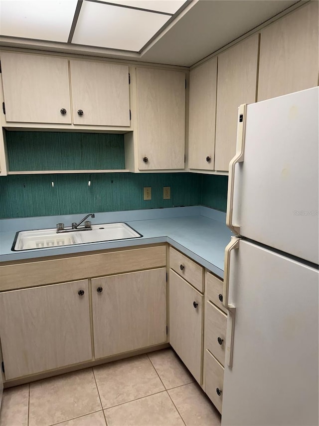 kitchen with light brown cabinetry, a sink, light countertops, freestanding refrigerator, and light tile patterned floors