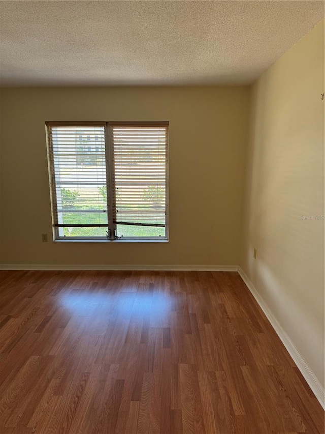 unfurnished room with baseboards, a textured ceiling, and wood finished floors
