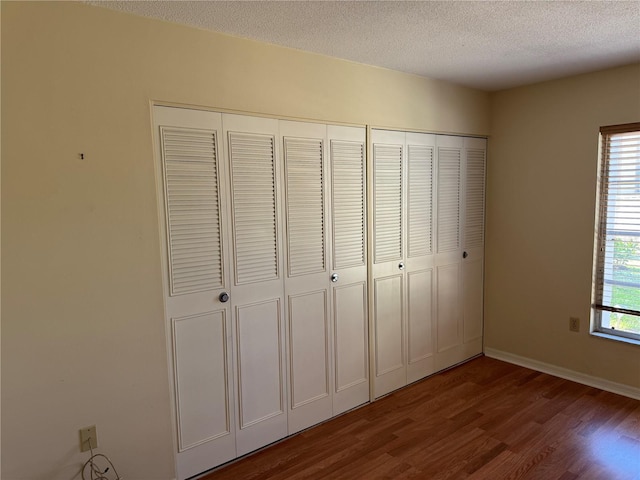 unfurnished bedroom featuring baseboards, two closets, dark wood finished floors, and a textured ceiling
