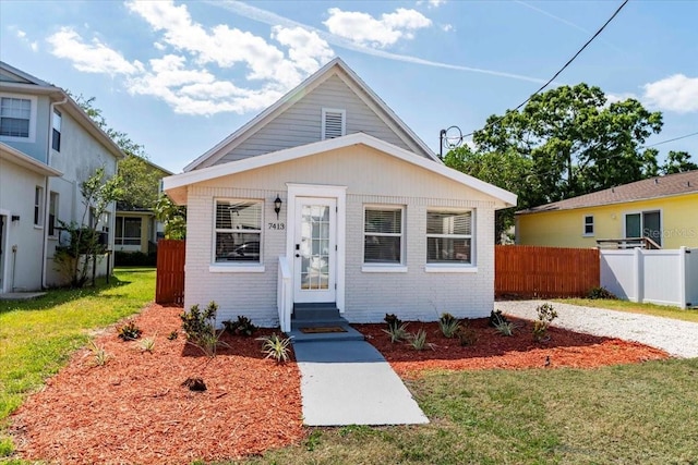 bungalow with a front lawn, fence, entry steps, and brick siding