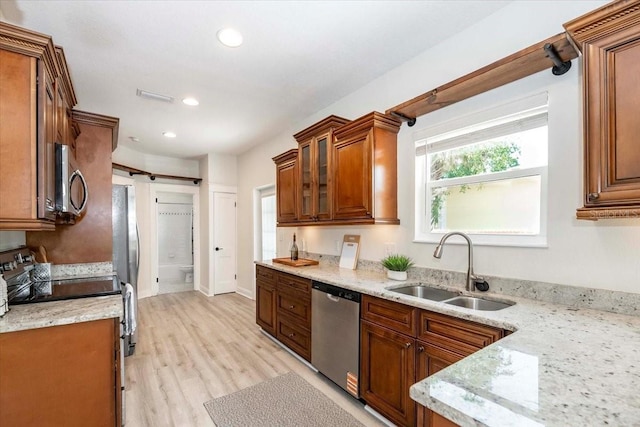 kitchen featuring a barn door, stainless steel appliances, brown cabinetry, a sink, and visible vents