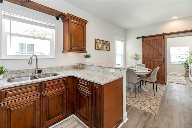 kitchen featuring a sink, light wood-style floors, a barn door, light stone countertops, and a peninsula