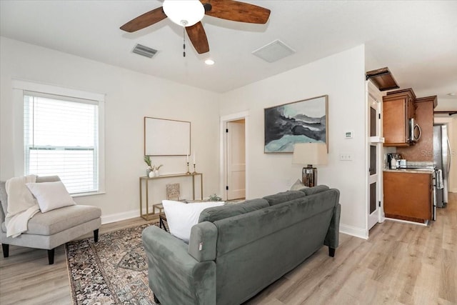 living room with baseboards, visible vents, light wood-type flooring, and ceiling fan