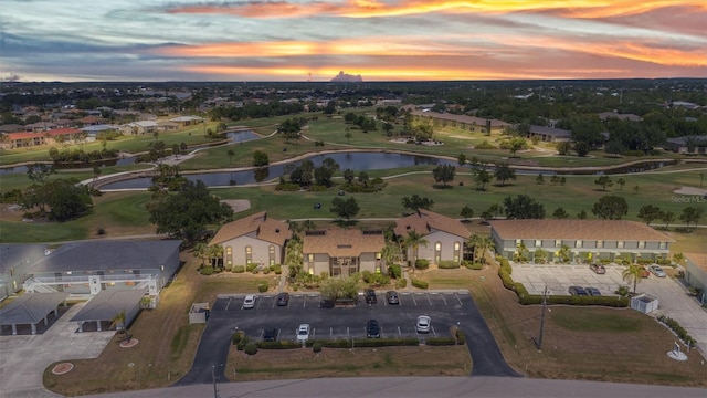aerial view at dusk with a water view, view of golf course, and a residential view