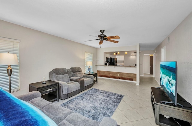 living area with light tile patterned flooring, ceiling fan, visible vents, and baseboards