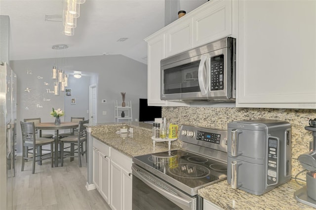 4129 Palisades Ave, North Port, FL 34287 - kitchen featuring vaulted ceiling, light stone counters, white cabinets, light wood finished floors, and stainless steel appliances