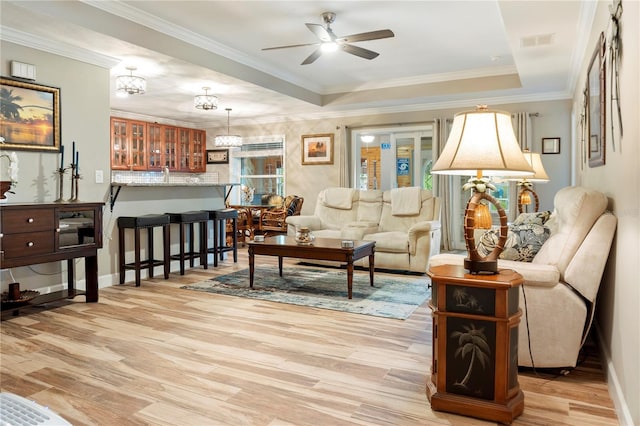 living room with light wood-style floors, ceiling fan with notable chandelier, baseboards, a tray ceiling, and visible vents
