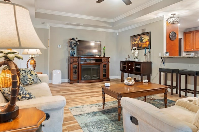 living room with a tray ceiling, baseboards, and light wood-type flooring