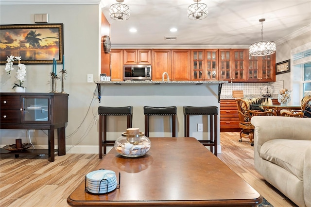 interior space with brown cabinetry, a kitchen bar, stainless steel microwave, light wood-style flooring, and a notable chandelier
