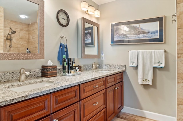 full bathroom featuring double vanity, tiled shower, a sink, and wood finished floors