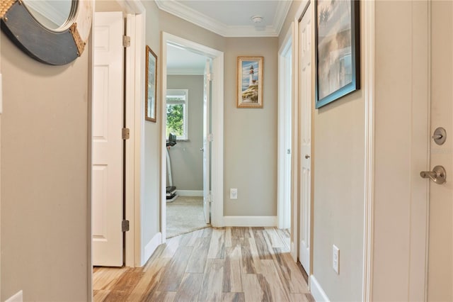 corridor featuring baseboards, ornamental molding, and light wood-style flooring