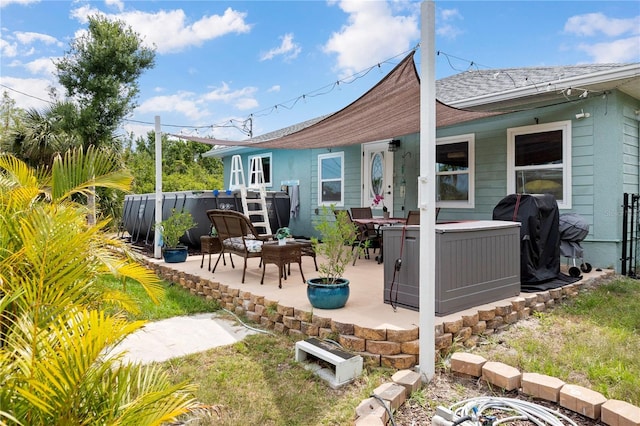back of house with a hot tub, a patio area, and roof with shingles