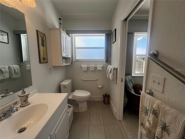 bathroom featuring toilet, baseboards, plenty of natural light, and vanity