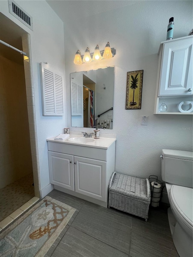 bathroom with visible vents, vanity, toilet, tile patterned floors, and a tile shower