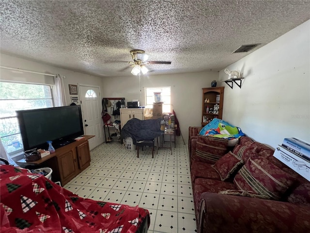 living area featuring light floors, a textured ceiling, visible vents, and a ceiling fan