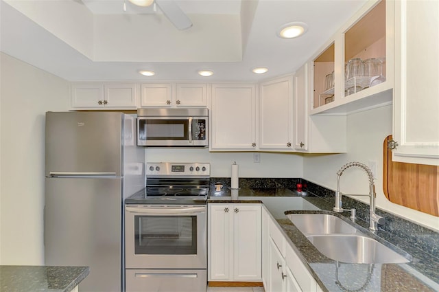 kitchen with stainless steel appliances, a sink, white cabinets, dark stone countertops, and glass insert cabinets