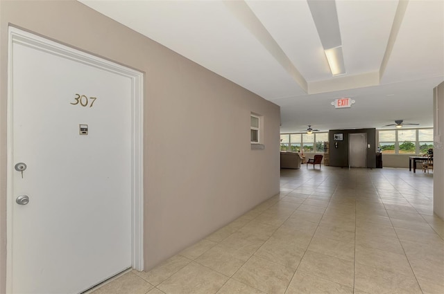 hall featuring light tile patterned flooring and a raised ceiling
